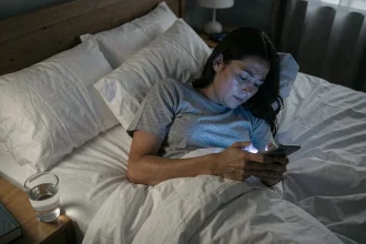 Femme fatiguée dans son lit la nuit qui consulte son smartphone, visage exposé à la lumière bleue de l'écran perturbant le sommeil